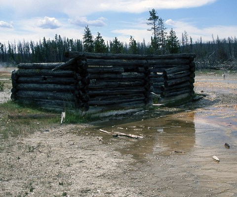 A dilapidated log building without a roof surrounded by thermal water