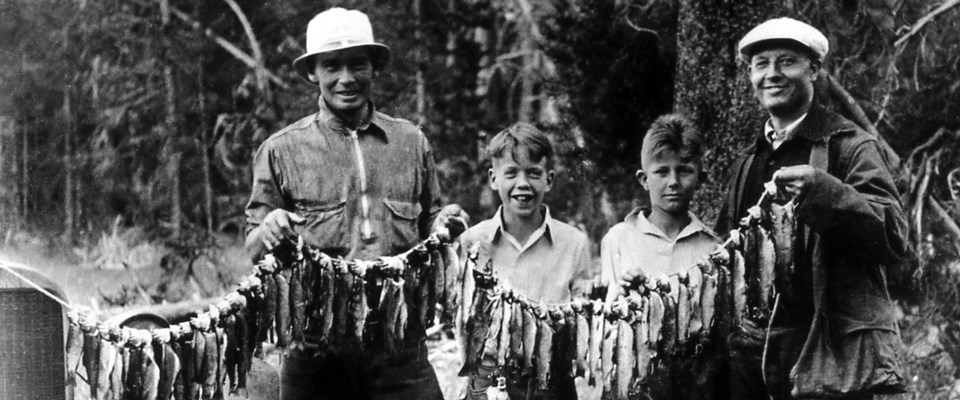 Two men and two boys hold a line of fish in a historic photo