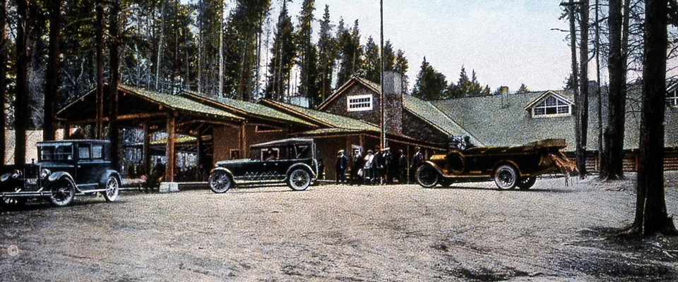 Early touring buses park in front of the entrance to a hotel in trees