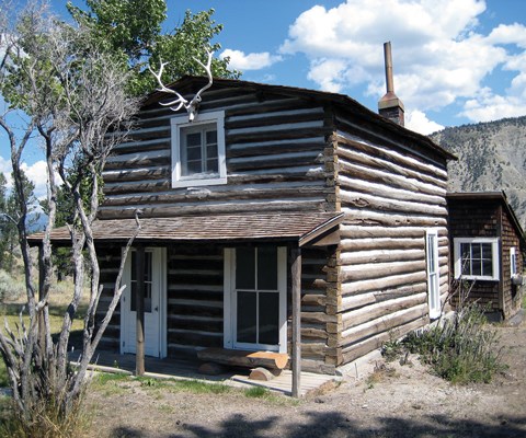 A two-story log cabin with porch and elk skull below the roof peak