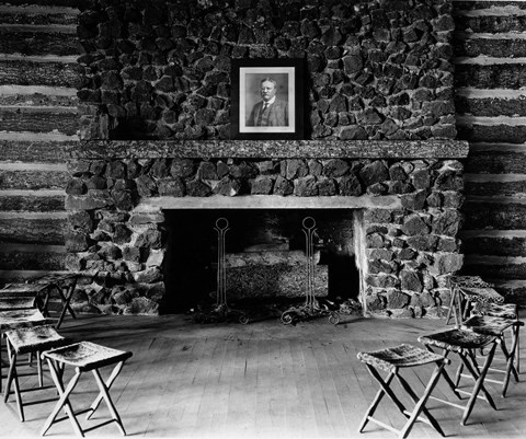 A portrait of President T. Roosevelt sits on the mantle of a stone fireplace with stools arranged in front of it