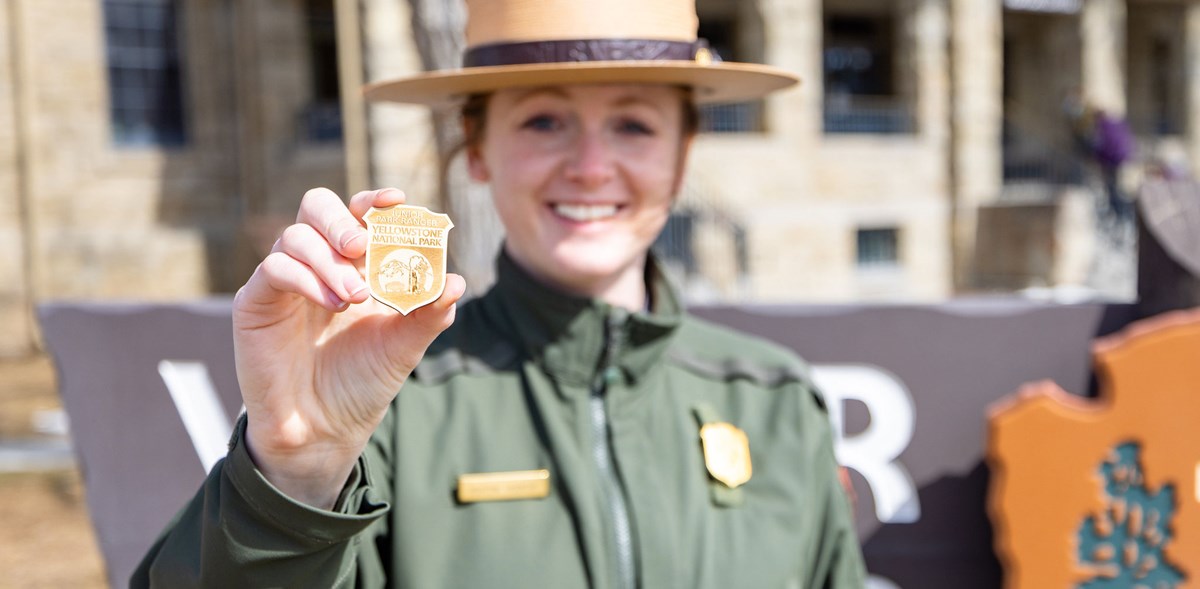 A park ranger holds ups a wooden junior ranger badge.