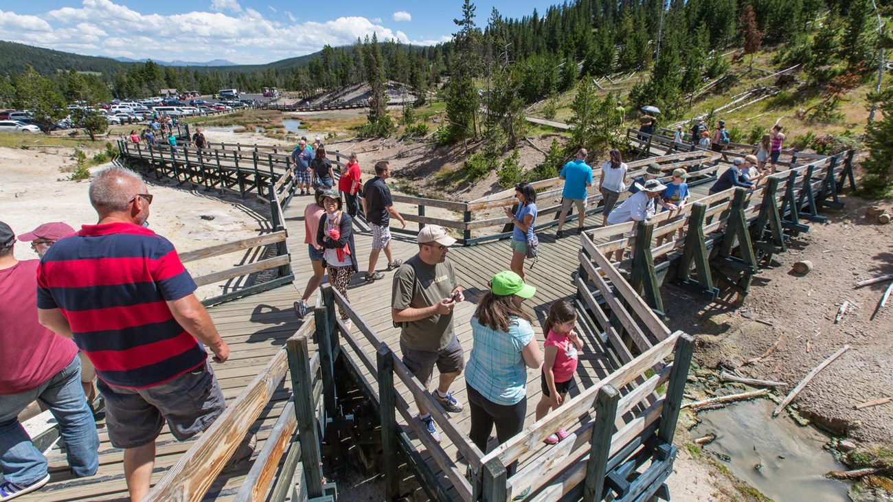 Crowds of people walking a wooden boardwalk in a thermal area