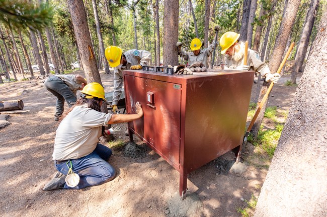 a group of people installing a bear-proof storage box in a campsite