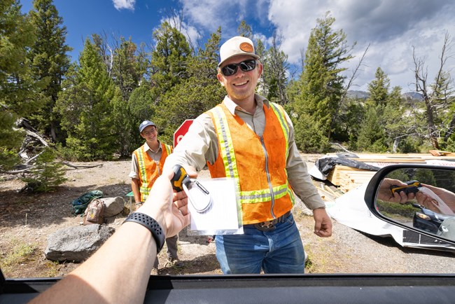 Person in vest hands a GPS to a vehicle driver