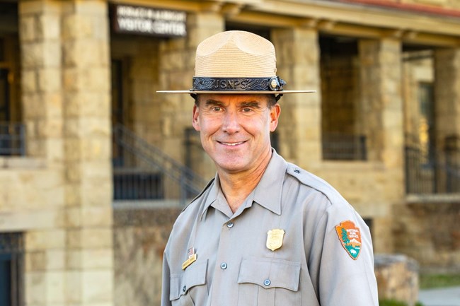 A man wearing a National Park Service uniform and flat hat who is smiling at the camera