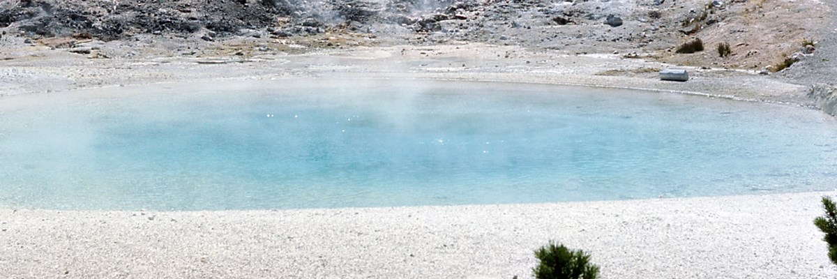 A blue steaming pool surrounded by pale rock