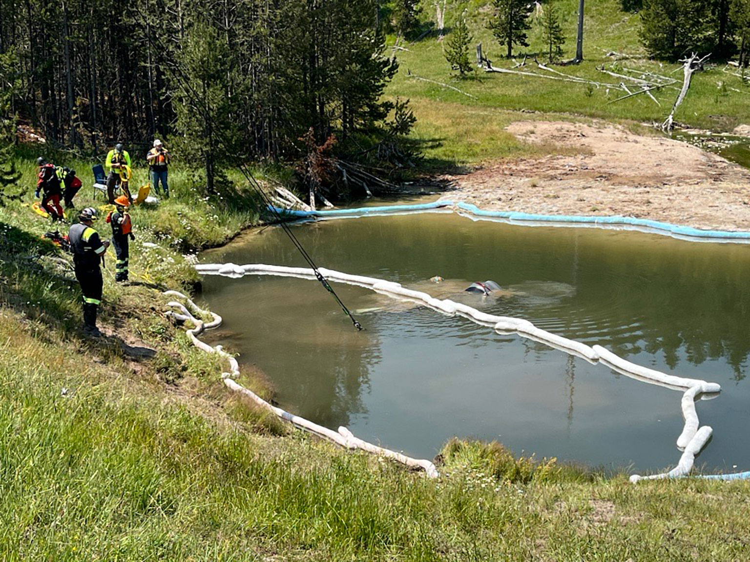 A crew of emergency personal retrieve a car underwater in a thermal feature.
