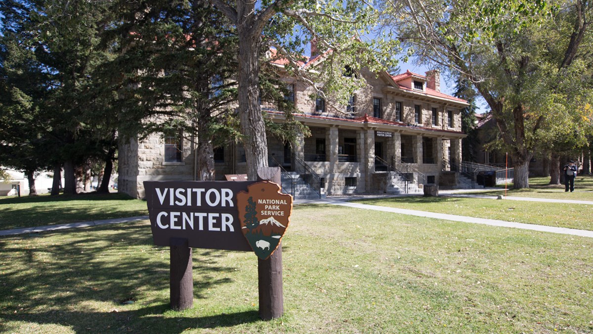 Brown wooden sign that reads "Visitor Center" stands in front of the two-story stone building.