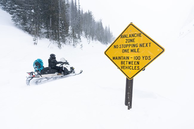 Snowmobiler riding past the avalance zone sign on Sylvan Pass