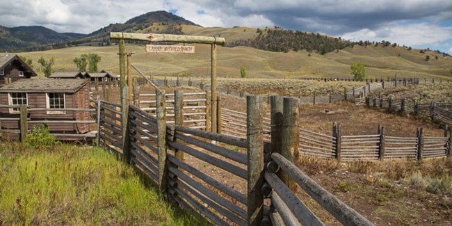 Tall wood fencing leads to the prominent entrance gate to historic cabins