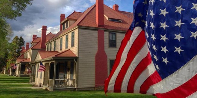 American flag in foreground with tan wooden homes with red chimneys and red tile roofs beyond.