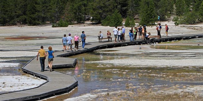 Visitors walk on a boardwalk that goes through a hydrothermal area
