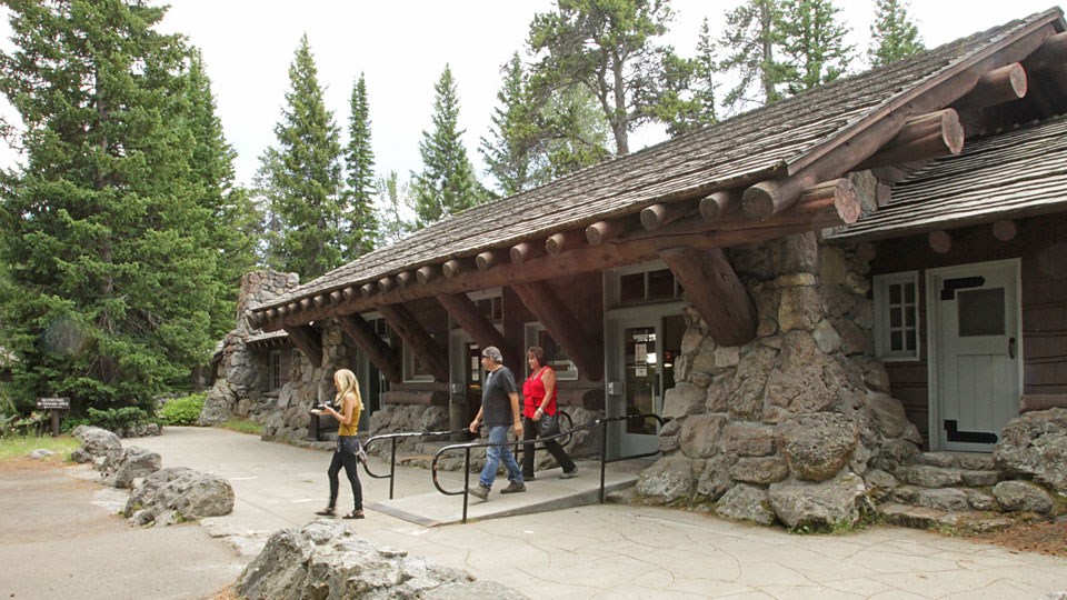 Three visitors leaving the single-story, stone and wood visitor center.