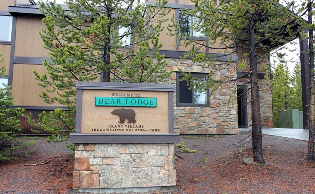 A stone lodge with the sign Bear Lodge, Grant Village out front