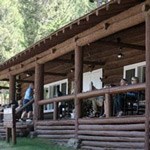 Visitors sit on the porch of a log cabin