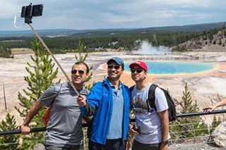 Three people take a selfie in front of a colorful hot springs