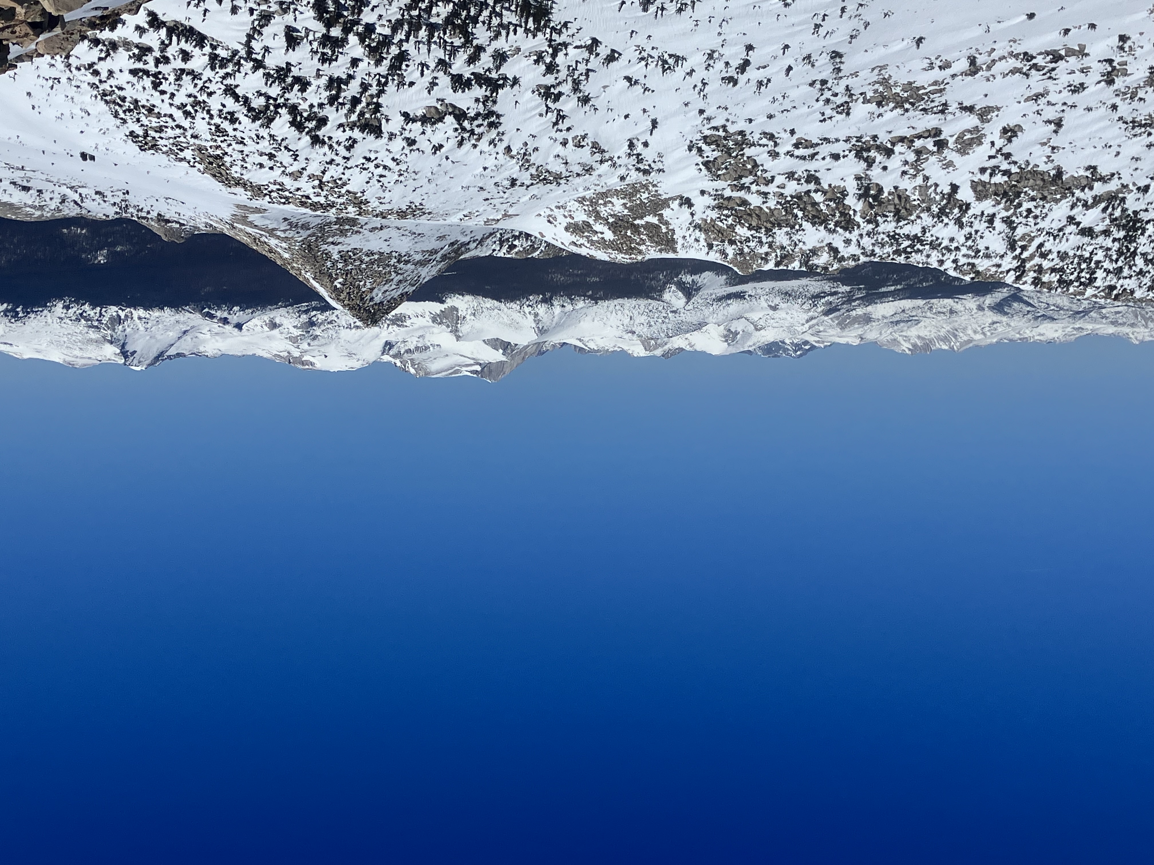 Overlooking snowy ride with a pyramid peak and beyond that to another chain of peaks, all mostly covered in snow