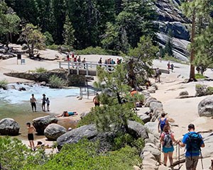 Visitors hiking along Mist Trail and wading in Merced River at the top of Nevada Fall.