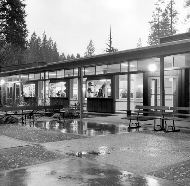 A paved courtyard with a low-slung building; the building is lit and curios are on display in several windows