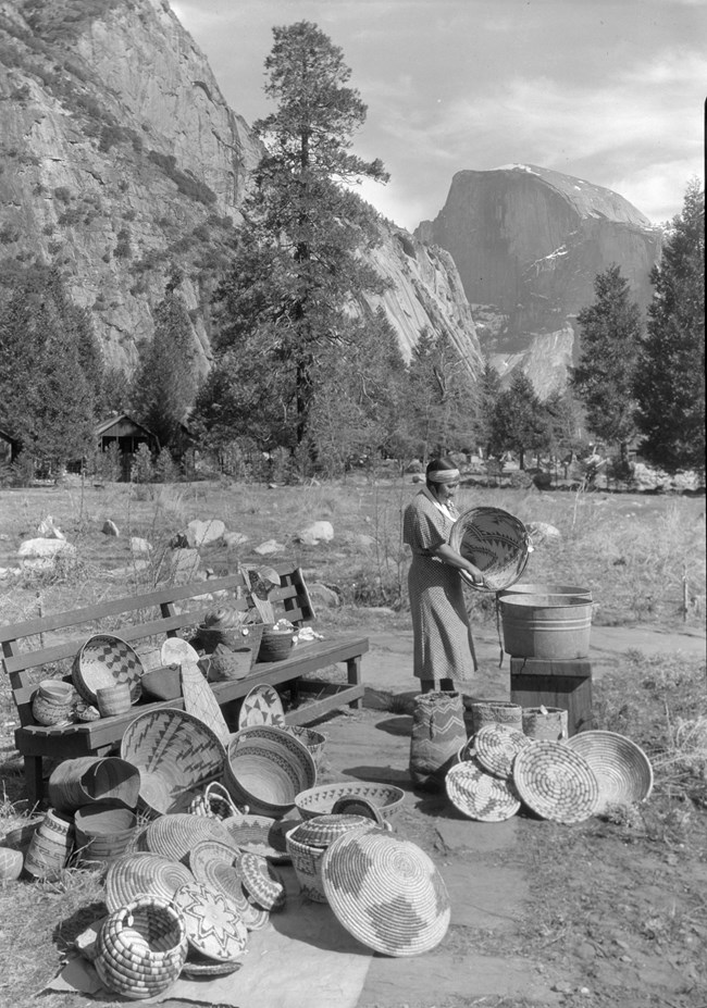 A woman stands next to a meadow with many woven baskets displayed around here