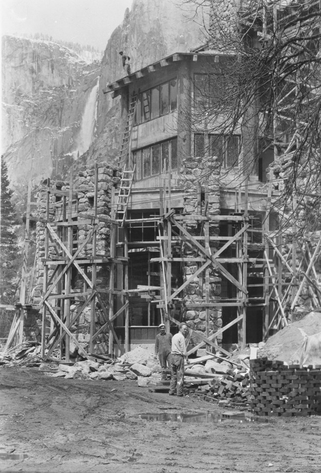 Workers surrounding a partially completed building, which has scaffolding and ladders around it