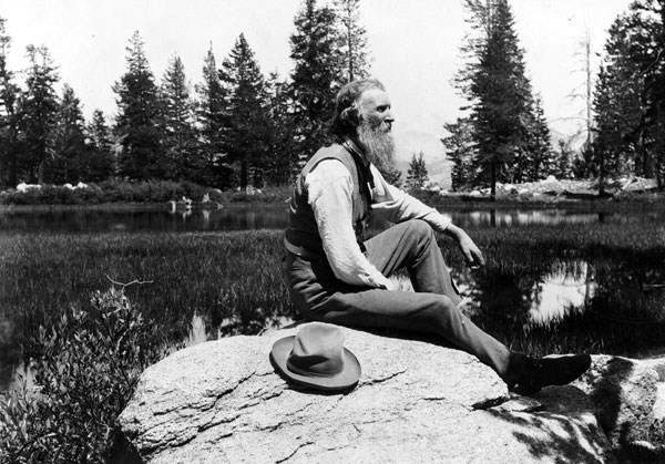 John Muir sits on rock with lake behind