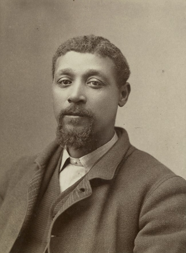 Black and white portrait of George Monroe, he is a Black man wearing a suit