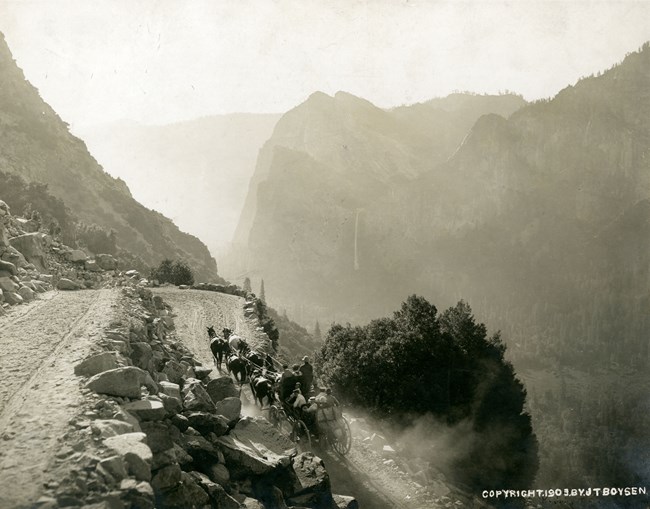 A six-horse stage travels uphill along steep switchbacks on an unpaved road