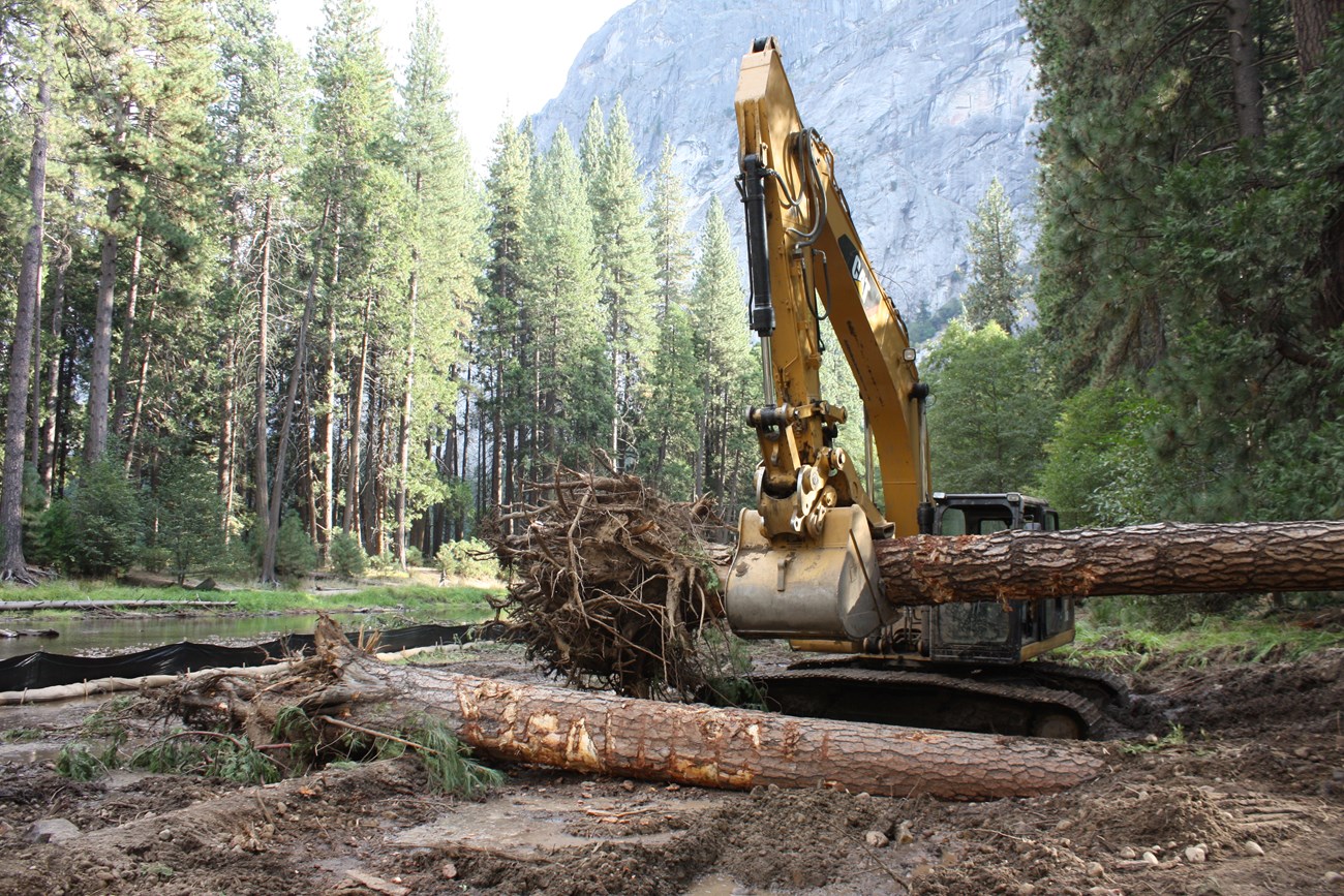 An excavator moves a piece of large wood into the river.