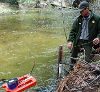 Ranger stands alongside river with water tester
