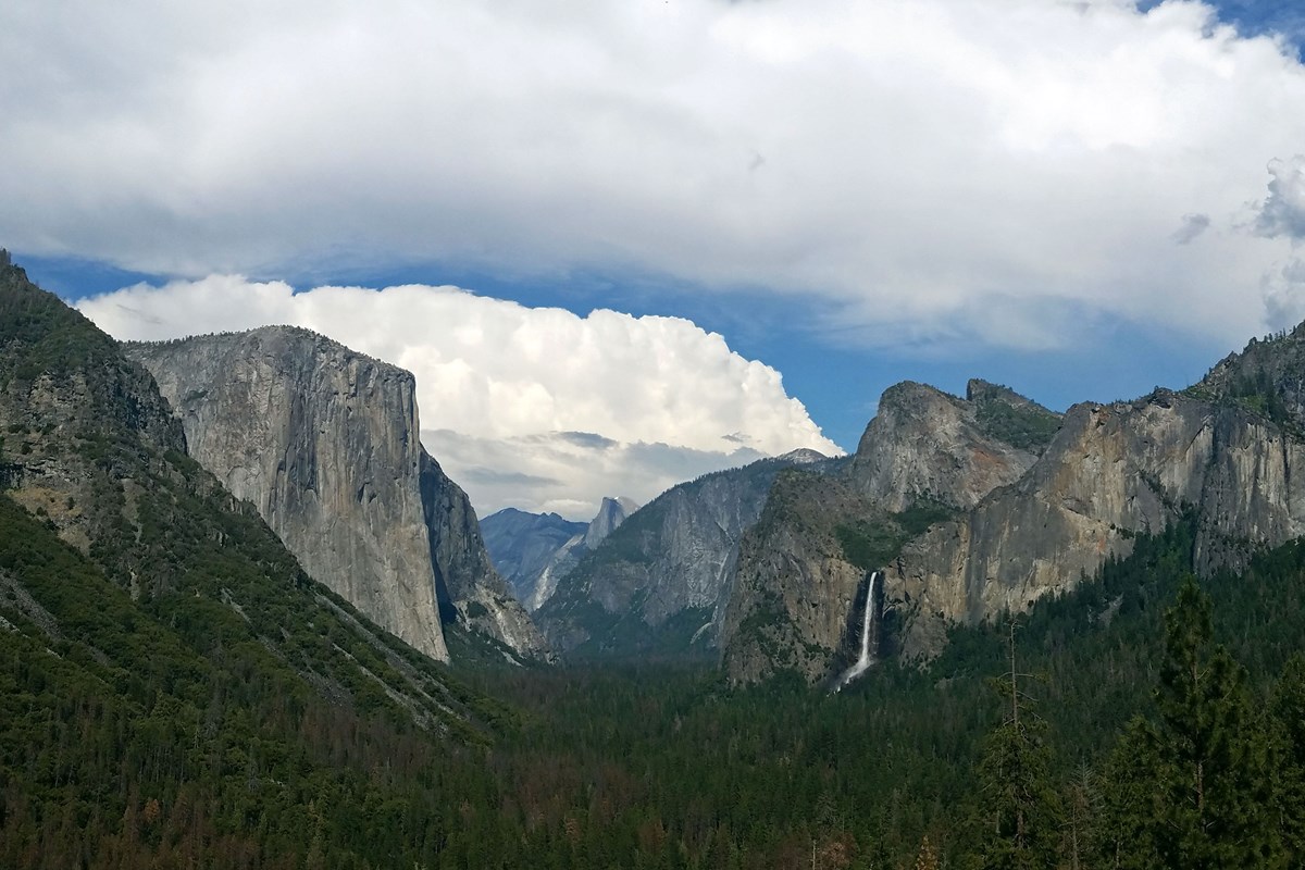 Soaring granite cliffs with waterfalls cascading down into a green, pine covered valley