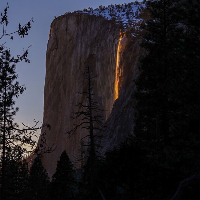 Wispy waterfall falling over a cliff, glowing orange with sunset light