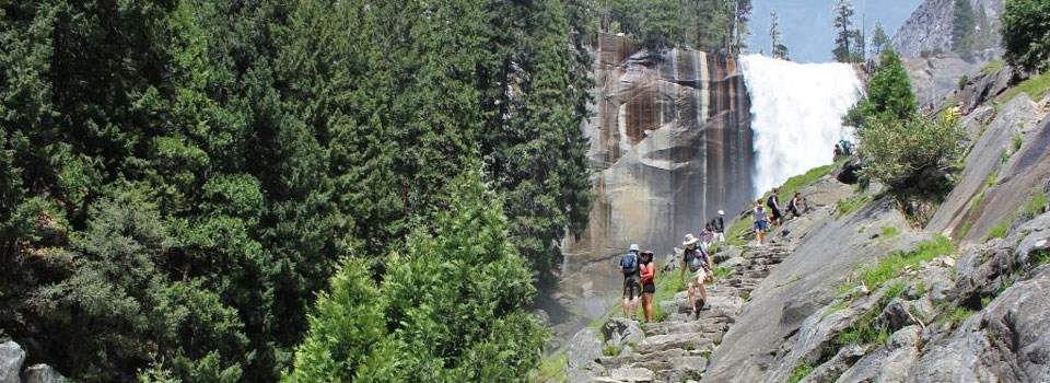 Hikers walking up granite steps towards a waterfall.