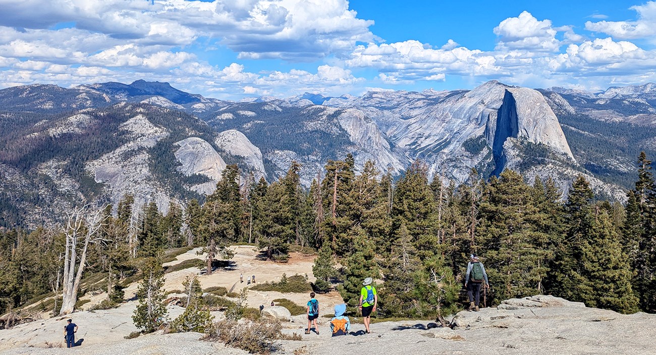 Visitors hike up and down Sentinel Dome, with Half Dome and the high Sierra visible in the background