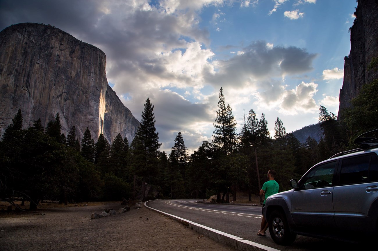 Car parked along Bridalveil straight with El Capitan in view and a person leaning on the hood.
