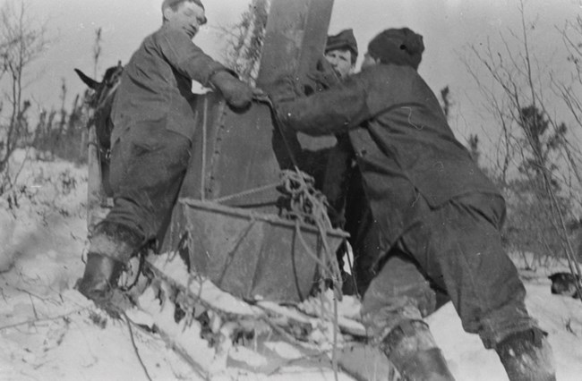 Historic photograph of men pushing a doghouse boiler uphill in winter