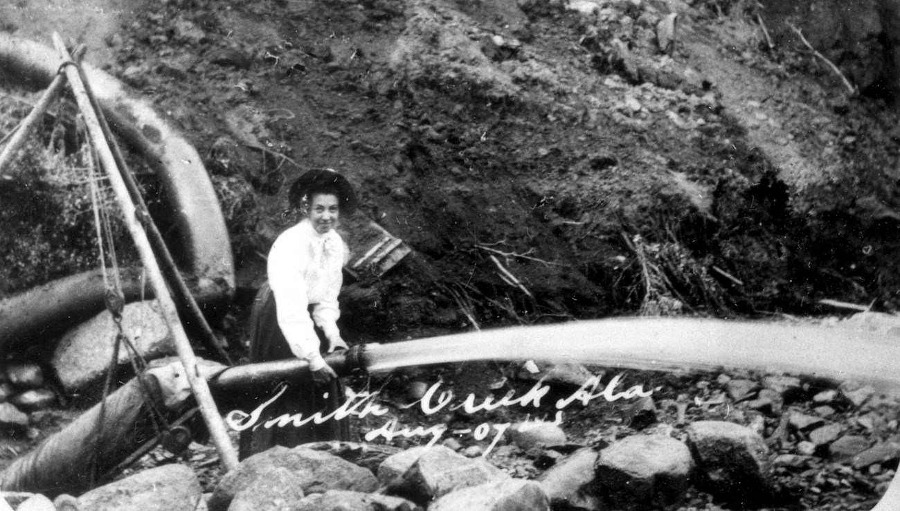 A woman demonstrates the use of a water canon for unearthing gold-rich gravels at Smith Creek just inside the Canadian border in Alaska’s 40-Mile mining district, August 1907