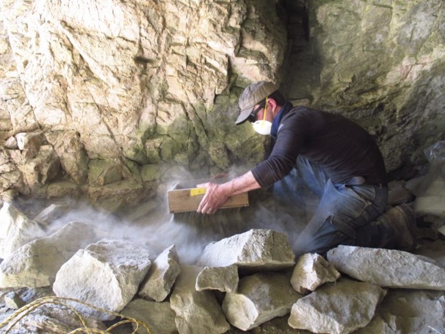 An archaeologist screens dirt in a cave.
