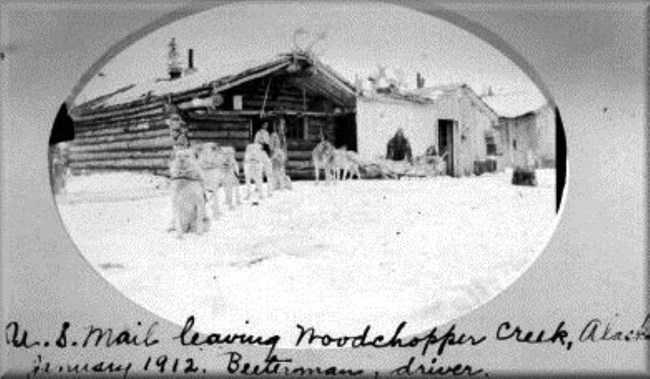 Yukon River mail carrier Ed Biederman and dog team at early Woodchopper Roadhouse buildings in 1912