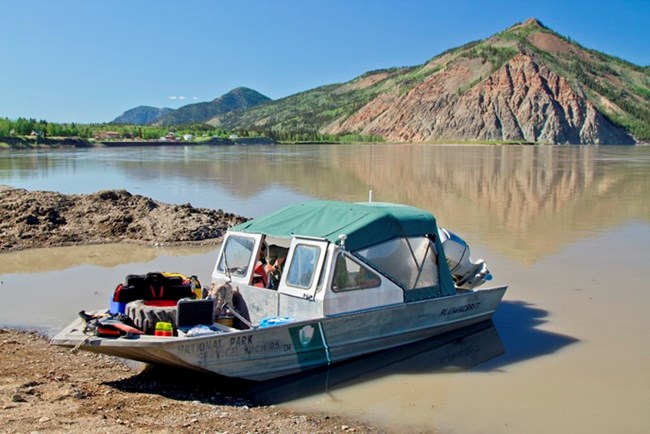 A motorboat on the bank of the Yukon River in Eagle, Alaska with Eagle Bluff in the background