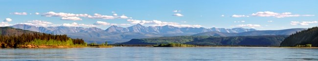 A panoramic photo of the Charley River mountains rising above the Yukon River on a clear day