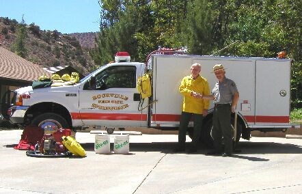 Two men in uniforms shake hands in front of a fire truck.