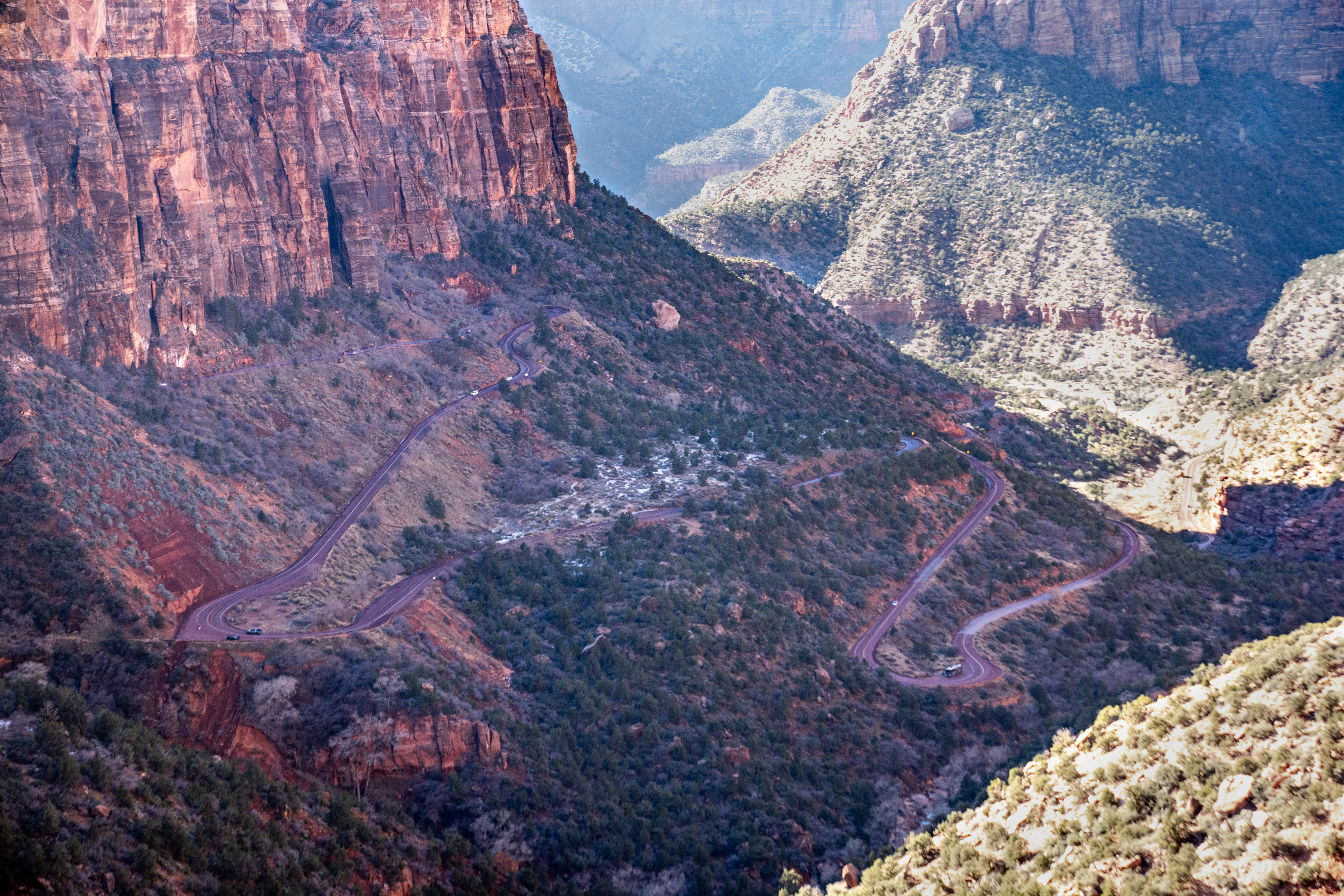 A long winding road on the side of a mountain with sandstone cliffs in the background.