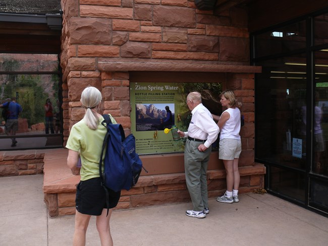 Three visitors fill their reusable water bottles at the Zion Canyon Visitor Center.