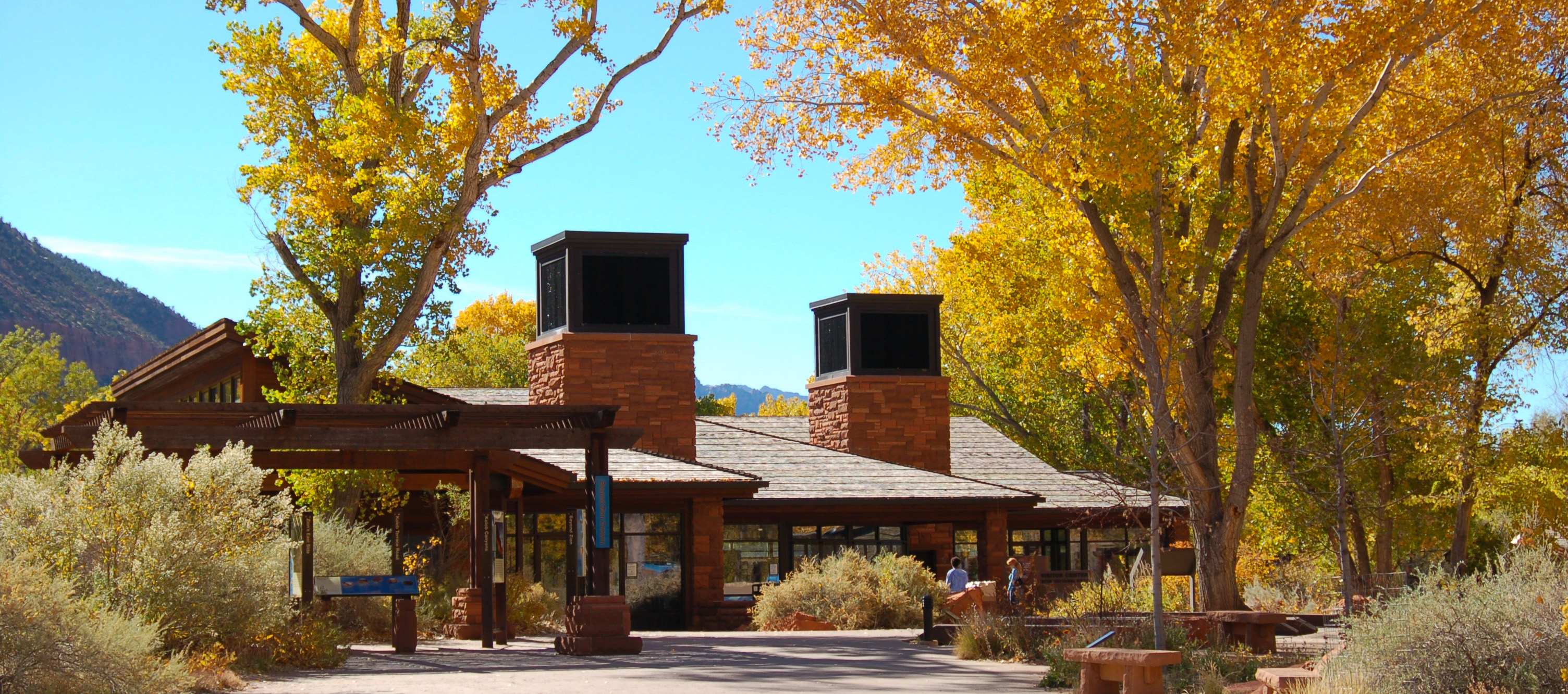 A stone and wood visitor center with yellow cottonwood trees overhead.