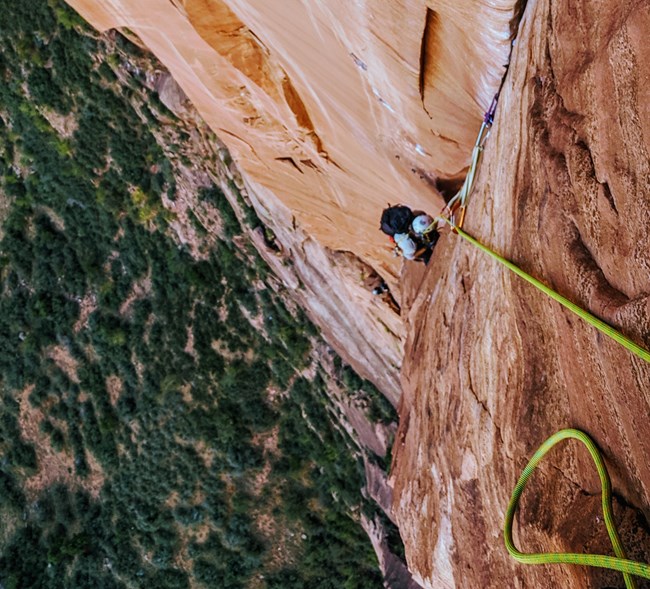 A climber ascends a rope on red walls